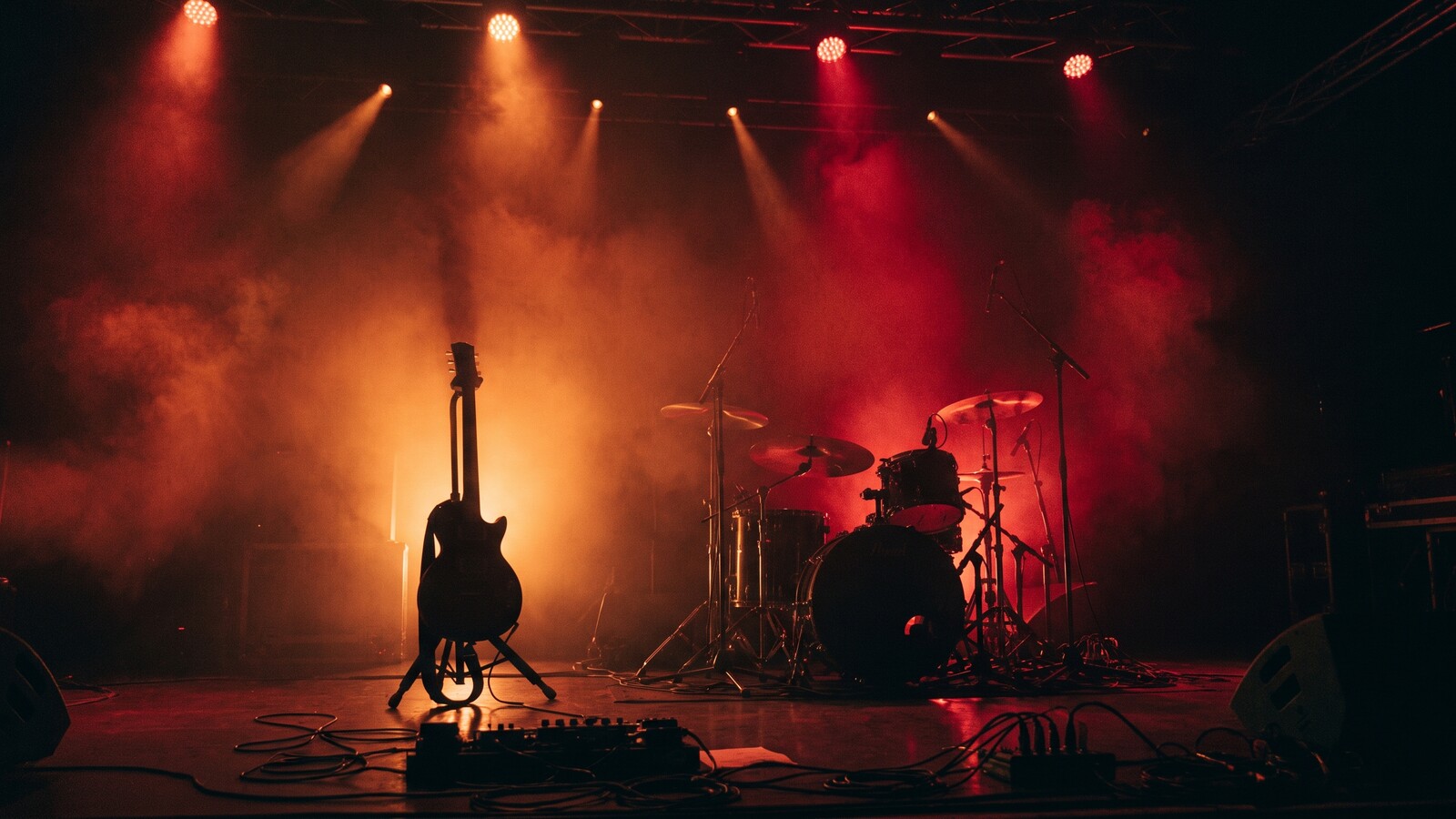 A guitar and drum kit on a dark stage in red light